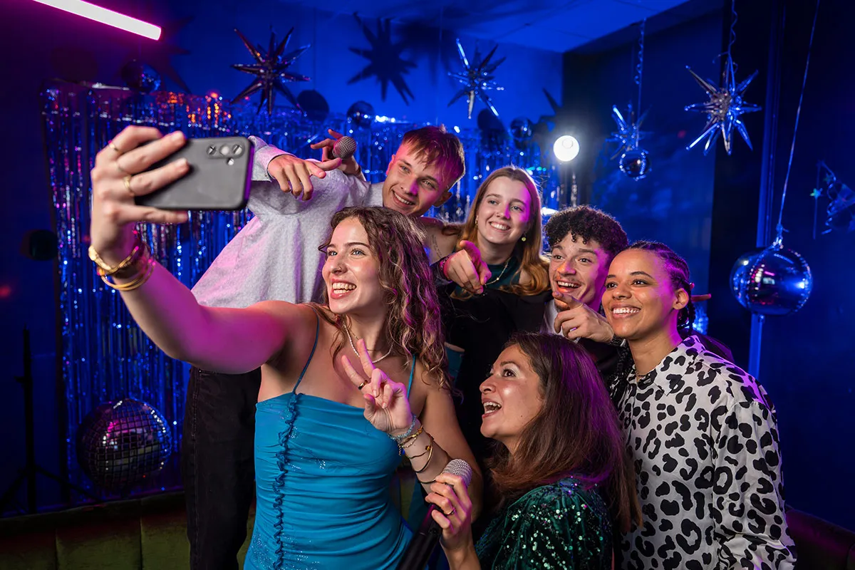Gruppe von Freunden posiert fuer selfie beim Karaoke
