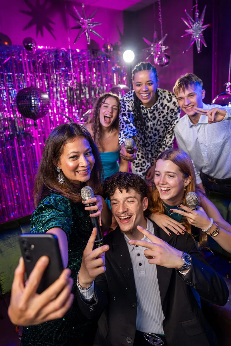Gruppe singt Karaoke mit Mikrofon in Party-Atmosphäre und macht selfies