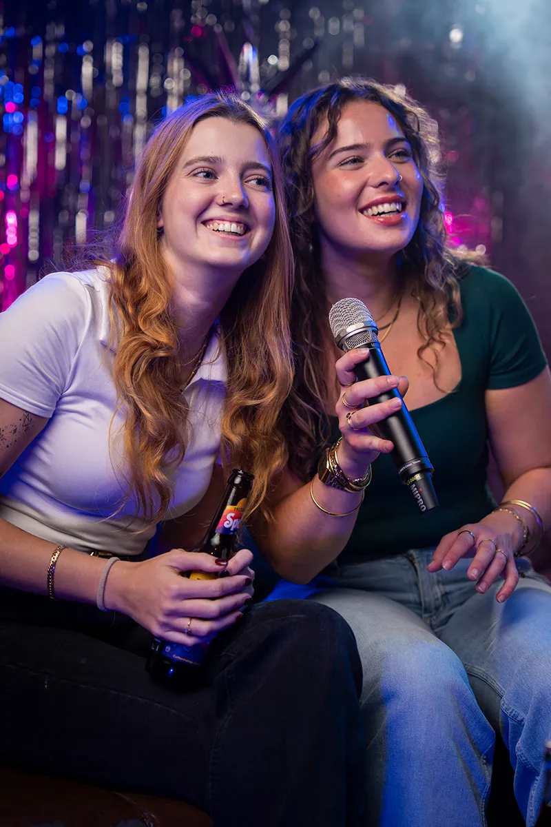 Freundinnen halten Mikrofone und lachen bei Karaoke