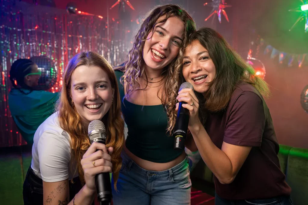 Freundinnen halten Mikrofone und lachen bei Karaoke